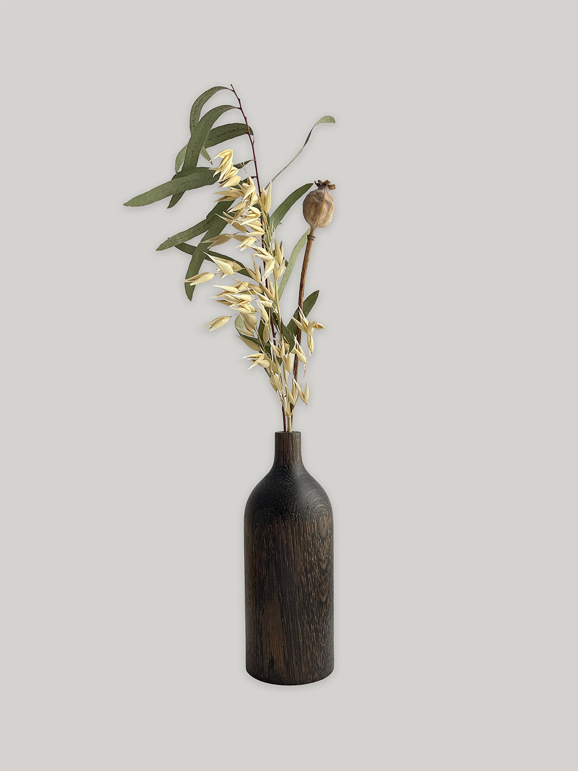 Dark wooden vase with dried flowers on a light grey background.