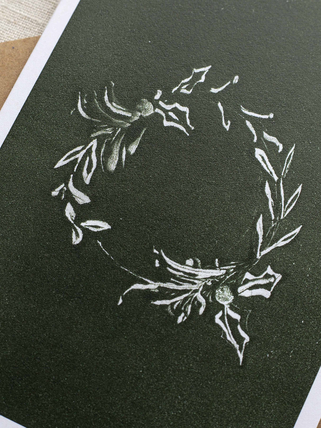 Close-up of botanical Christmas card with a leafy wreath design on a green background.