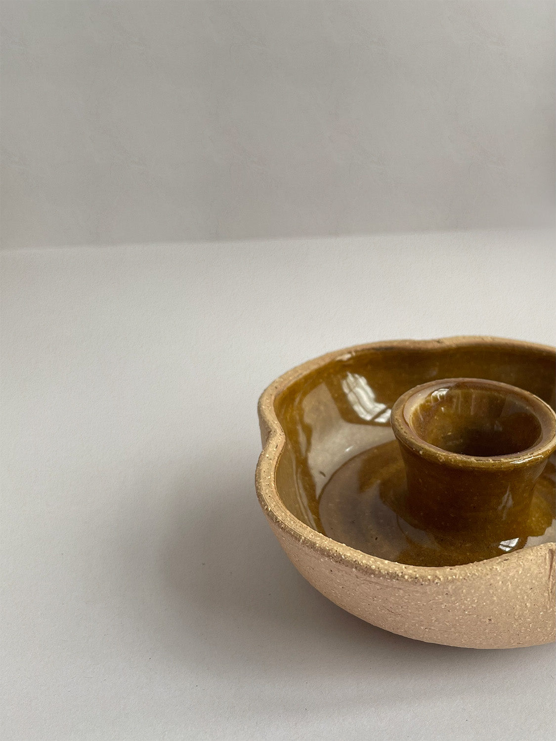 A hand-thrown ceramic candle holder in a rustic yellow ochre glaze on a neutral background - front view close-up.