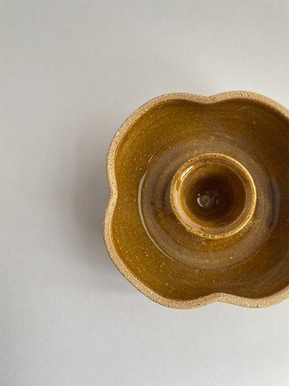 A hand-thrown ceramic candle holder in a rustic yellow ochre glaze on a neutral background - top view close-up.