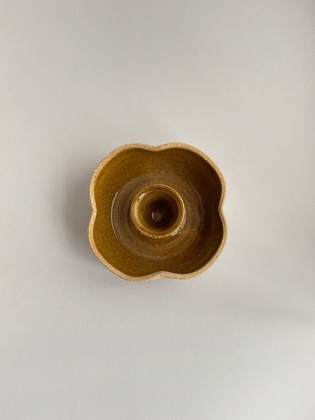 A hand-thrown ceramic candle holder in a rustic yellow ochre glaze on a neutral background - top view.