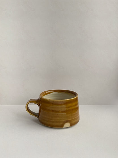 A golden yellow handmade ceramic espresso mug with a handle, on a neutral background - right side view.