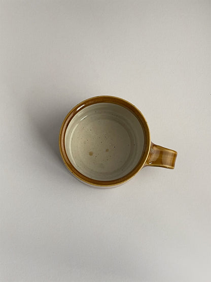 A golden yellow handmade ceramic espresso mug with a handle, on a neutral background - top view.