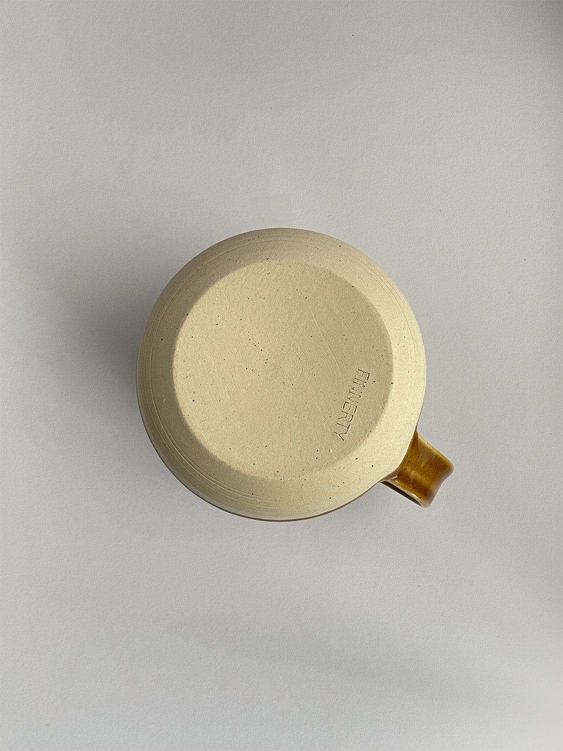 A golden yellow handmade ceramic jug with a curved body and a handle, on a neutral background - base view.