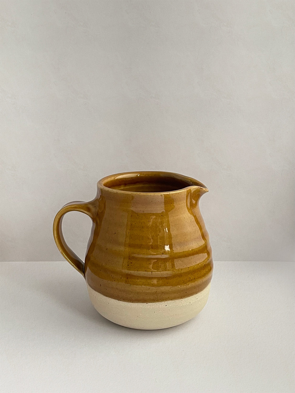 A golden yellow handmade ceramic jug with a curved body and a handle, on a neutral background - right side view.
